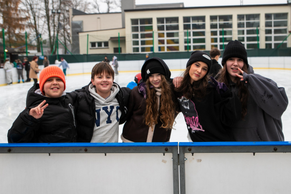 Młodzież na lodowisku stoi przy bandzie