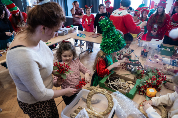 Uczestnicy warsztatów mikołajkowych przy stanowiskach, mama z córką przygotowują stroik 