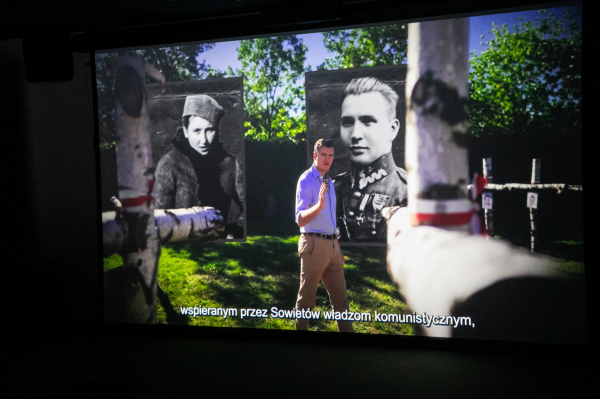 Kadr z filmu - mężczyzna na tle zdjęć żołnierzy