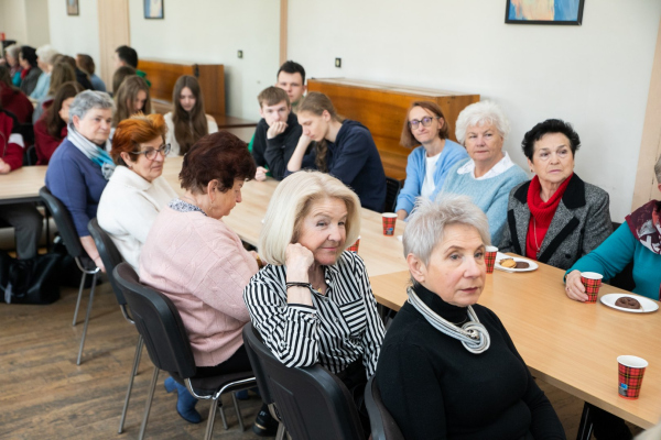Seniorzy i młodzież siedzący przy stołach 