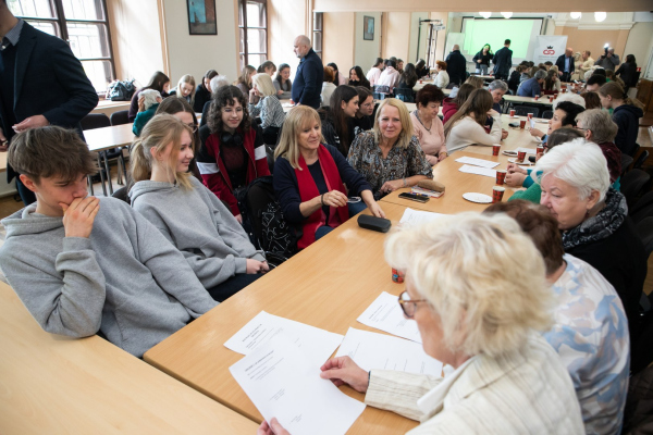 Seniorzy i młodzież siedzący przy stołach 