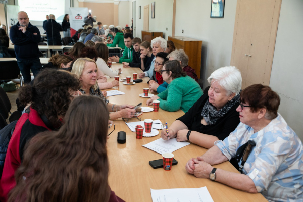 Seniorzy i młodzież siedzący przy stołach 