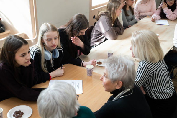 Seniorzy i młodzież siedzący razem przy stole, rozwiązujący zadanie