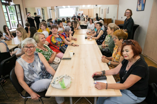 Seniorzy i młodzież siedzący przy stołach 