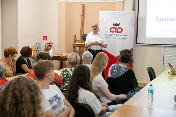 Młodzież siedząca przy stołach, w tle przemawiający dyrektor CKiS 